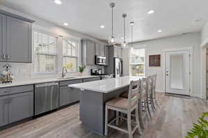 Kitchen featuring gray cabinets, light wood-style floors, appliances with stainless steel finishes, a kitchen bar, and recessed lighting