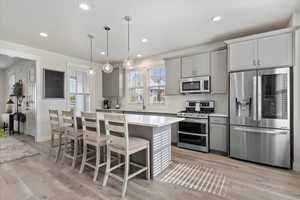 Kitchen with gray cabinetry, stainless steel appliances, a breakfast bar area, recessed lighting, and pendant lighting