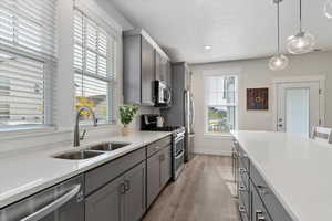 Kitchen with gray cabinetry, appliances with stainless steel finishes, light stone countertops, and hanging light fixtures