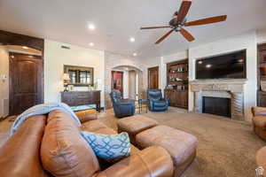 Carpeted living area with a textured ceiling, arched walkways, built in features, a premium fireplace, and ceiling fan
