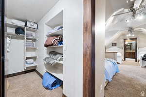 Walk in closet featuring light colored carpet, a ceiling fan, and vaulted ceiling