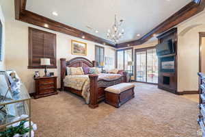 Bedroom featuring a raised ceiling, access to exterior, light colored carpet, a large fireplace, and crown molding