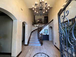 Entrance foyer featuring arched walkways, a high ceiling, a chandelier, a textured wall, and stairway