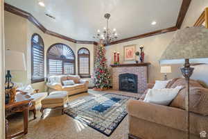Living room with ornamental molding, a textured wall, a chandelier, a brick fireplace, and carpet flooring