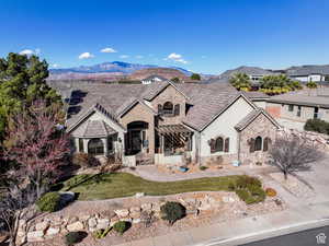 French country style house with stone siding, covered porch, stucco siding, a mountain view, and a front yard