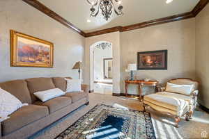Living area with ornamental molding, arched walkways, a textured wall, a chandelier, and carpet floors