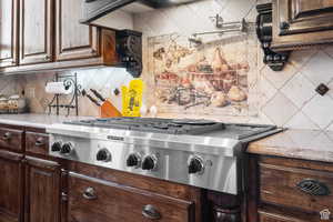 Kitchen featuring decorative backsplash, stainless steel gas stovetop, light stone counters, and dark brown cabinetry