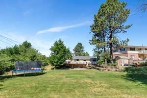 View of grassy yard with a trampoline and a deck