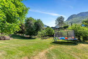 View of green lawn featuring a trampoline and a mountain view