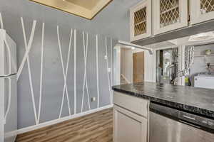 Kitchen with dishwasher, freestanding refrigerator, light wood-style flooring, washer / clothes dryer, and white cabinets