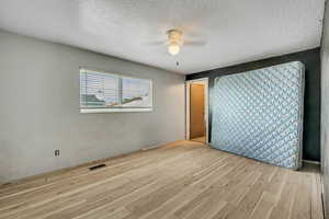 Unfurnished room featuring a textured ceiling, light wood-type flooring, and ceiling fan