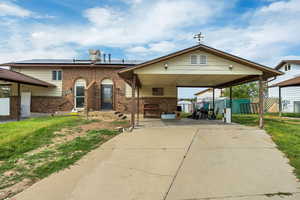 View of front facade with a patio area, brick siding, concrete driveway, solar panels, and a carport
