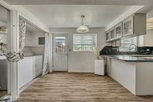 Kitchen featuring light wood-type flooring, a textured ceiling, washing machine and clothes dryer, decorative light fixtures, and a peninsula