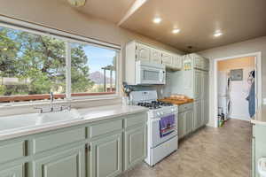 Kitchen with white appliances, a mountain view, light countertops, estacked washer and dryer, and white cabinets