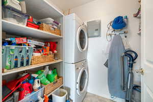 Washroom featuring stacked washer / drying machine, electric panel, and light tile patterned floors
