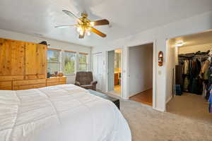 Carpeted bedroom with a walk in closet, a ceiling fan, and ensuite bathroom