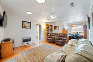 Living room featuring light wood-type flooring, heating unit, and a ceiling fan