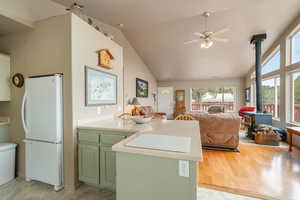 Kitchen featuring a peninsula, green cabinets, a wood stove, freestanding refrigerator, and light countertops