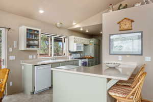 Kitchen featuring a peninsula, white appliances, recessed lighting, vaulted ceiling, and a kitchen breakfast bar