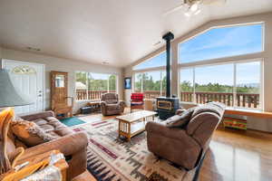 Living room with a wood stove, wood finished floors, a ceiling fan, and high vaulted ceiling