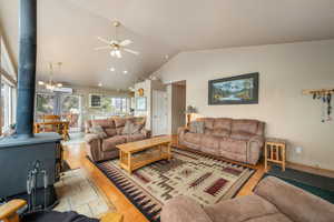 Living area featuring a wood stove, wood finished floors, high vaulted ceiling, ceiling fan, and a wall mounted air conditioner