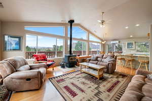 Living area featuring a wood stove, wood finished floors, high vaulted ceiling, and ceiling fan