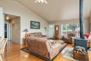Living area featuring a wood stove, lofted ceiling, light wood-type flooring, and ceiling fan