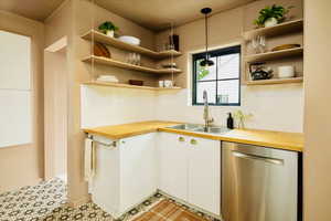 Kitchen with wood counters, stainless steel dishwasher, open shelves, and white cabinetry