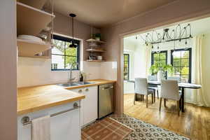 Kitchen with decorative light fixtures, tasteful backsplash, white cabinets, light wood-style floors, and dishwasher