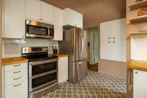 Kitchen with stainless steel appliances, backsplash, white cabinetry, and wooden counters
