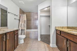 Bathroom featuring two vanities, tiled shower / bath, light tile patterned floors, a spacious closet, and a textured ceiling