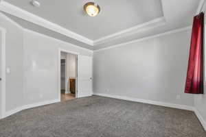 Unfurnished bedroom featuring a raised ceiling, carpet flooring, crown molding, and connected bathroom