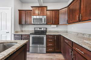 Kitchen with appliances with stainless steel finishes, light stone countertops, light wood finished floors, and dark brown cabinetry