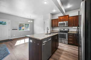 Kitchen featuring stainless steel appliances, a textured ceiling, a kitchen island with sink, light stone counters, and light wood finished floors