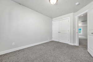 Unfurnished bedroom with carpet floors, a closet, and a textured ceiling