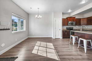 Kitchen featuring stainless steel appliances, a chandelier, pendant lighting, light stone countertops, and light wood-type flooring
