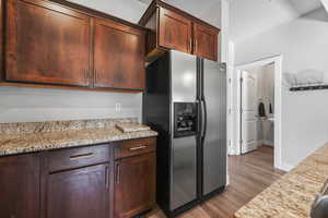 Kitchen featuring stainless steel fridge with ice dispenser, light stone counters, dark wood finished floors, and dark brown cabinets