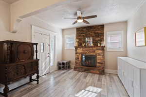 Living area featuring light wood-type flooring, a fireplace, a ceiling fan, a textured ceiling, and crown molding