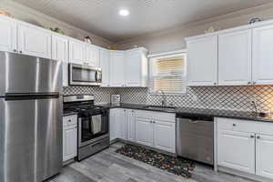 Kitchen with stainless steel appliances, ornamental molding, white cabinetry, backsplash, and dark stone counters