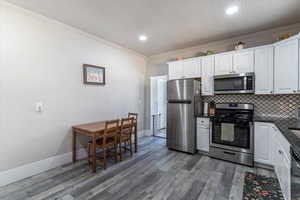 Kitchen featuring appliances with stainless steel finishes, white cabinets, ornamental molding, backsplash, and light wood finished floors