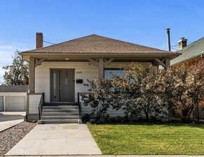 View of front facade with covered porch, a chimney, a front yard, and a shingled roof