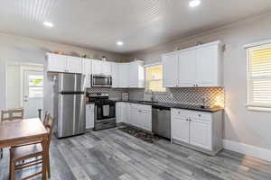 Kitchen featuring stainless steel appliances, white cabinets, crown molding, backsplash, and light wood-style floors