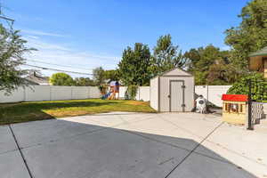 Fenced backyard featuring a playground, a storage unit, and a patio