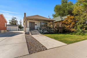 View of front of house featuring an outdoor structure, covered porch, a chimney, a front yard, and a detached garage