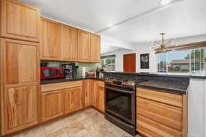 Kitchen with stainless steel gas stove, a chandelier, backsplash, beam ceiling, and dark stone counters