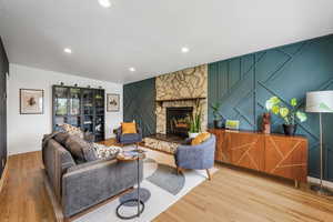 Living area with a decorative wall, light wood-type flooring, a stone fireplace, and recessed lighting