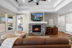 Living room featuring a raised ceiling, a fireplace, wood finished floors, ceiling fan, and recessed lighting