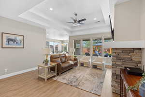 Living area with a tray ceiling, light wood finished floors, recessed lighting, and a ceiling fan