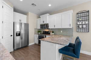 Kitchen with stainless steel appliances, backsplash, white cabinets, a peninsula, and dark wood-style flooring