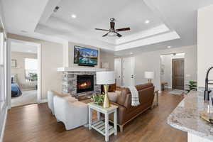 Living room featuring wood finished floors, a fireplace, recessed lighting, ceiling fan, and a tray ceiling